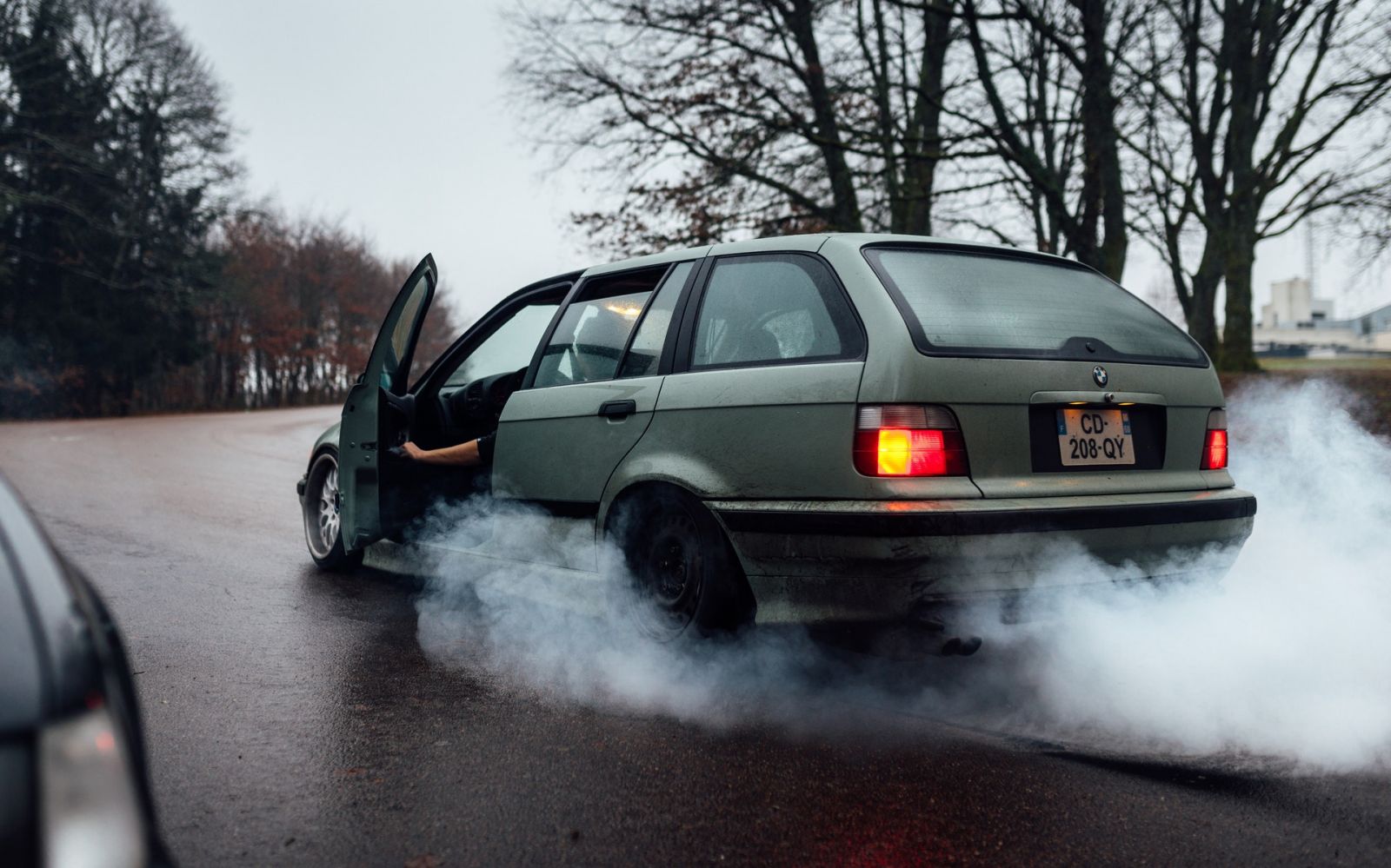 Broken car on the road with white smoke coming out of it. 